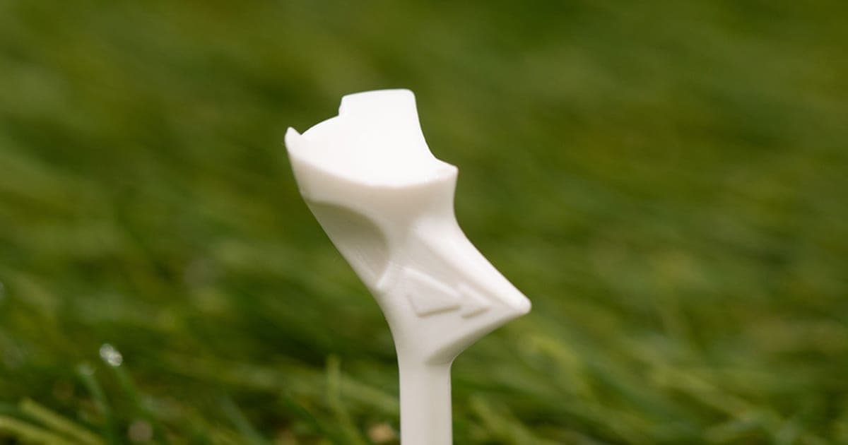 White FlightPath golf tee with an arrow-shaped head pushed into green grass